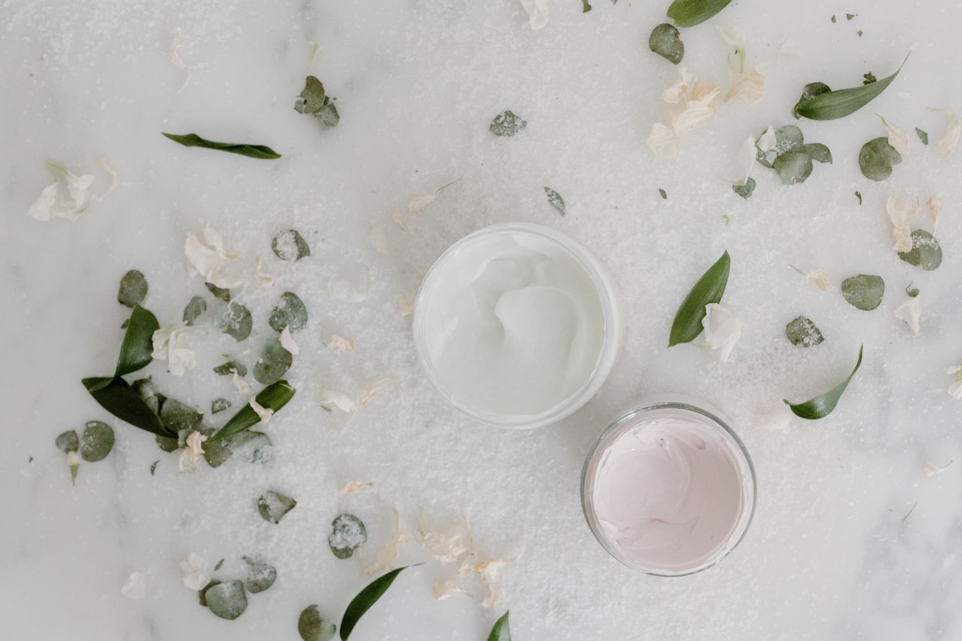 Flat lay of cosmetic cream jars surrounded by natural leaves and petals — Korean beauty skincare collection