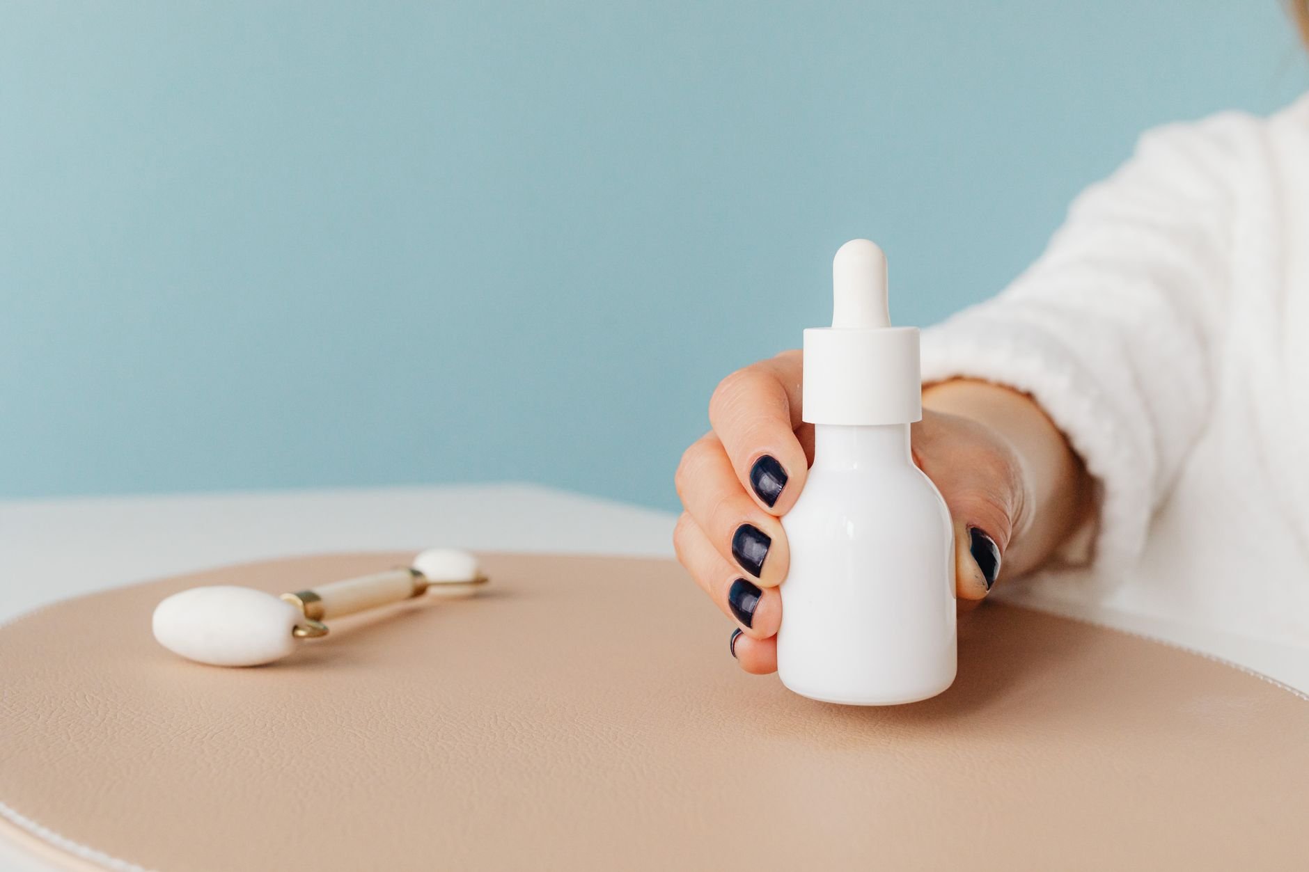 Close-up of a hand holding a serum bottle with a jade roller — Korean skincare ritual